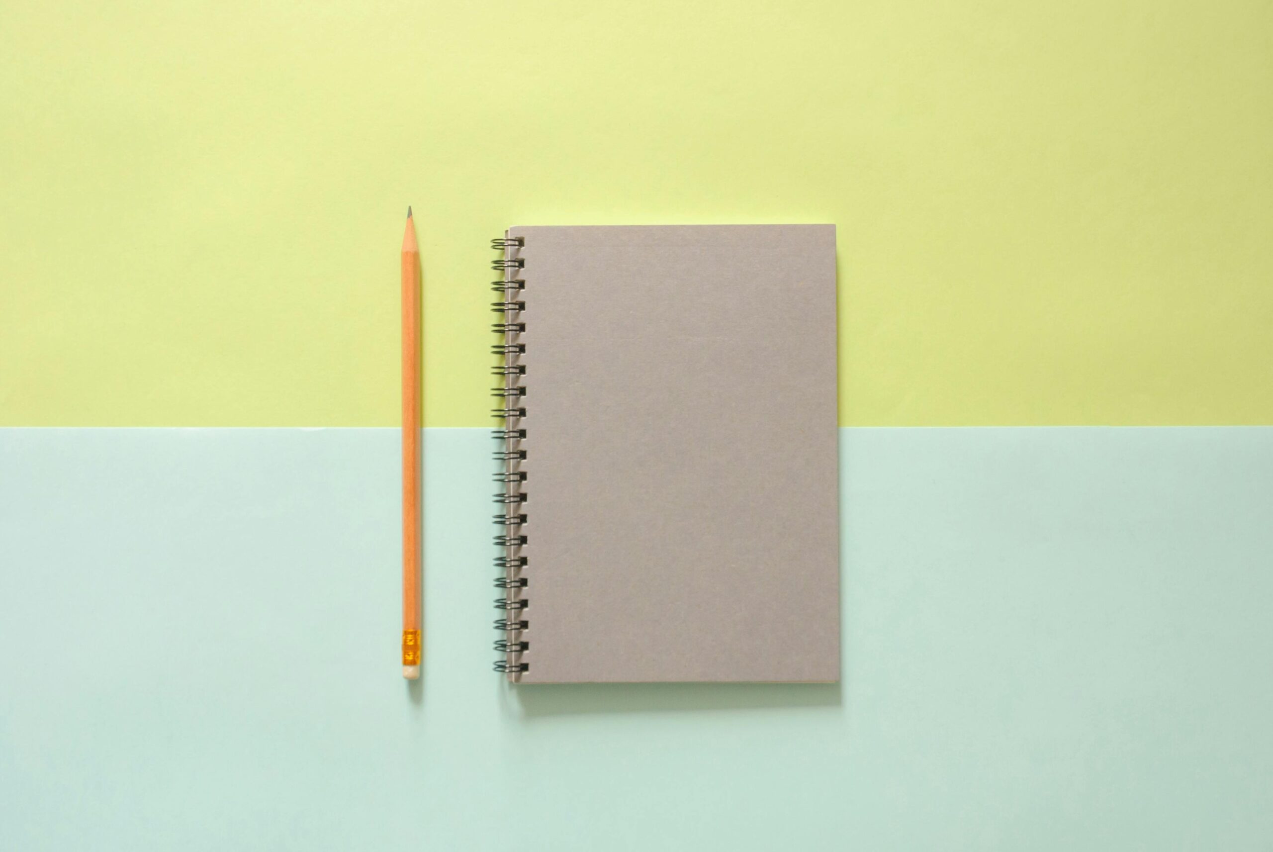 Flat lay of a spiral notebook and pencil on a pastel background, ideal for school and office themes.