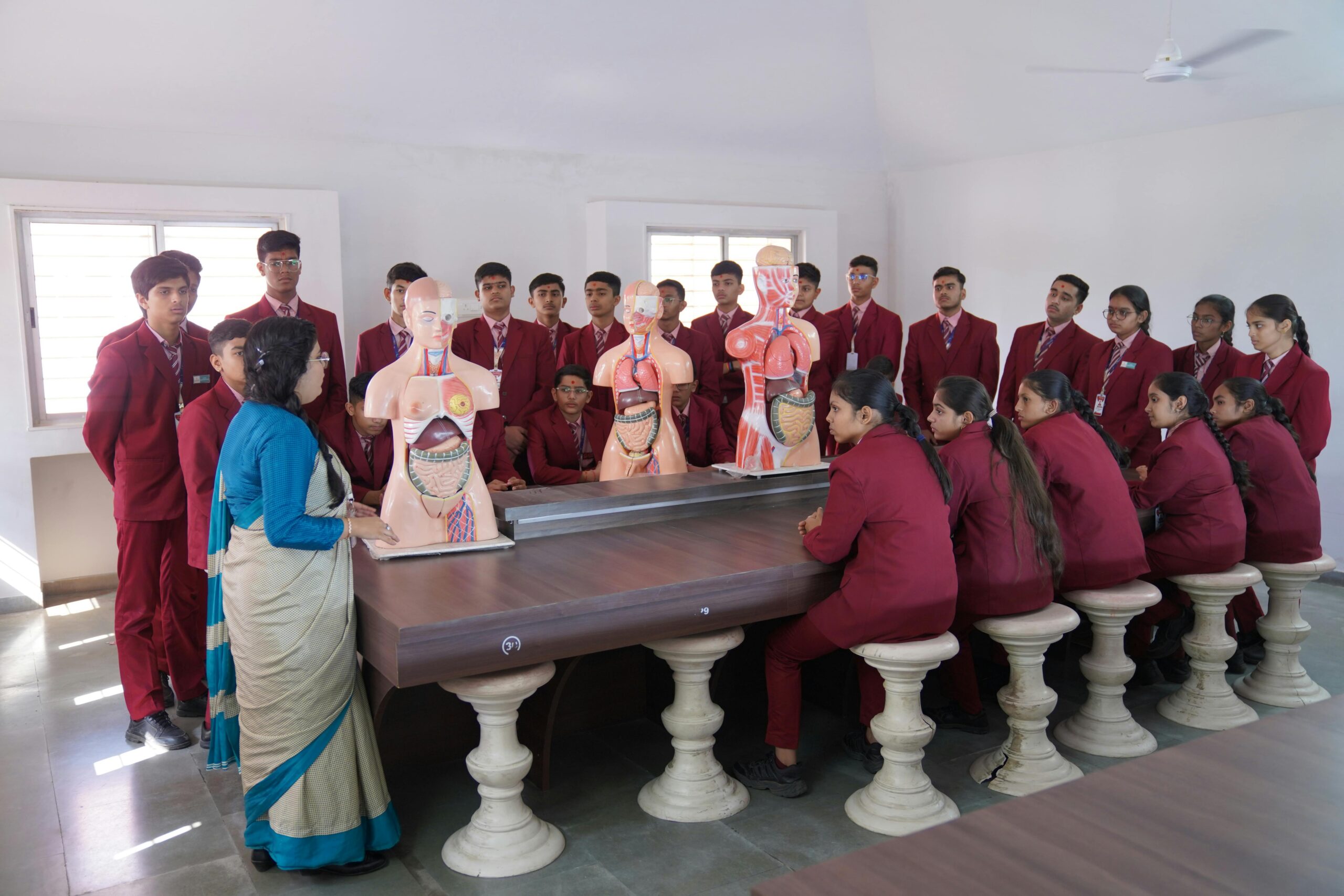 Students in Petlad, India studying anatomy with models in a classroom.